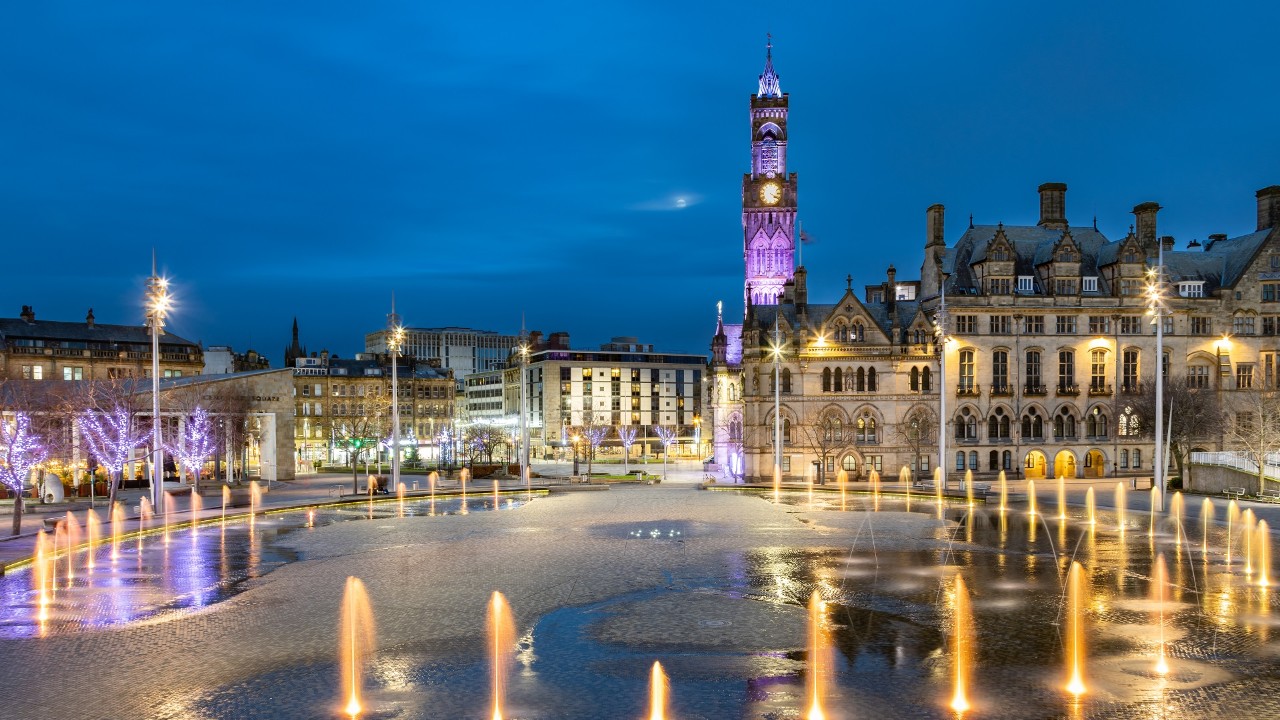 Dramatic night shot of Bradford City Hall reflected in the mirror pool in the city park.